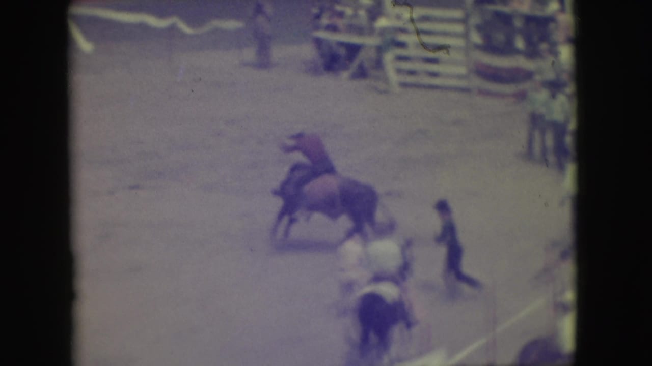 1949 Denver rodeo frame showing a cowboy on a bucking bull, with arena assistants and horseback figures nearby.