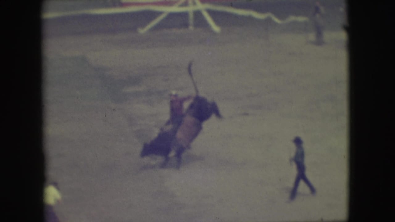 1949 Denver rodeo frame with the bull mid-buck, the rider tilted backward, and an arena assistant walking nearby.