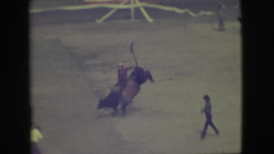 1949 Denver rodeo frame with the bull mid-buck, the rider tilted backward, and an arena assistant walking nearby.