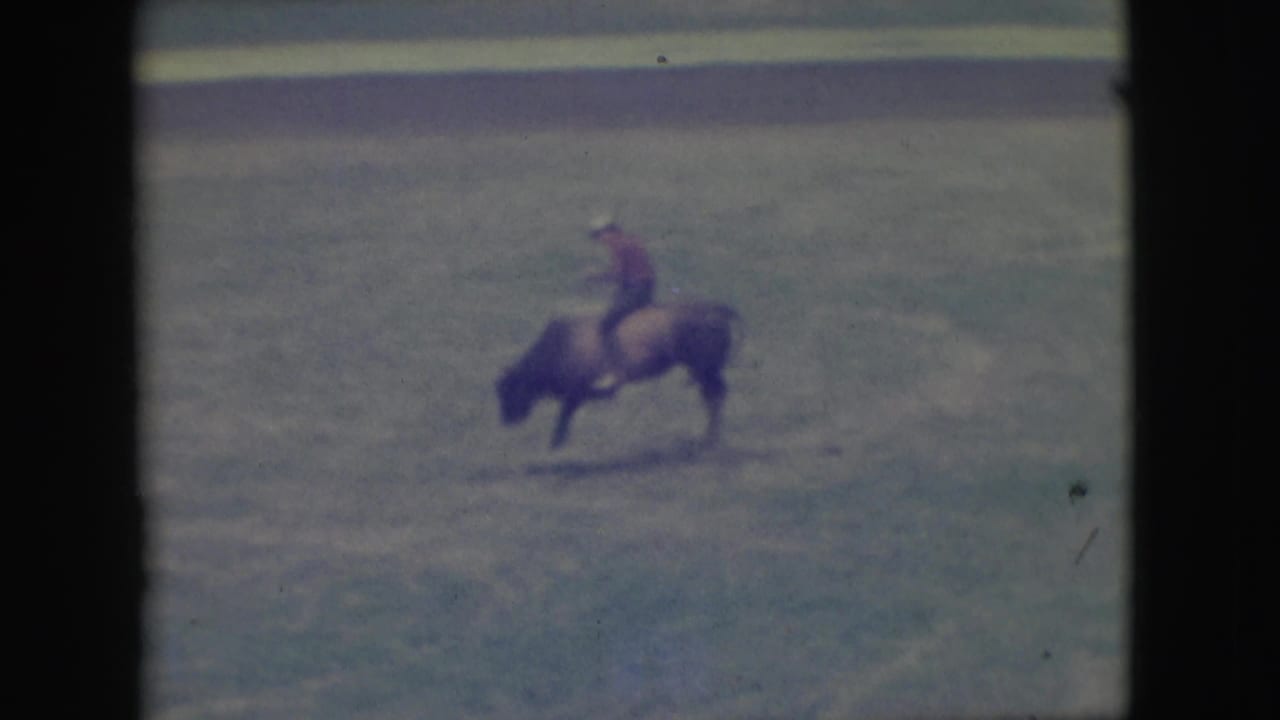 Rider on a bull in a distant rodeo arena view.