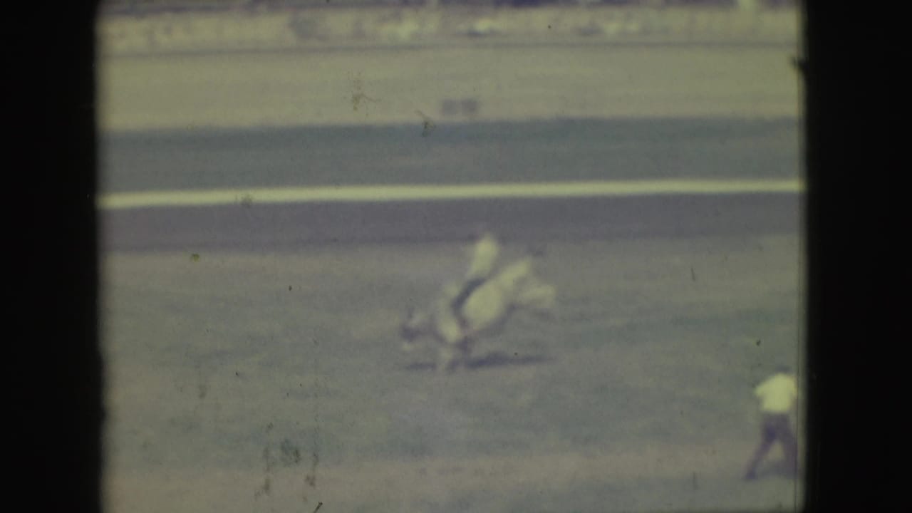 In 1949 Denver footage, a horse and rider cross a distant dirt arena while a crowd watches from behind fencing.