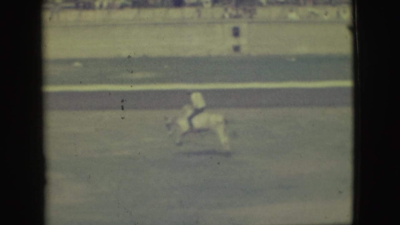 The rider continues across the Denver arena, seen through soft, faded 8mm color with spectators in the background.