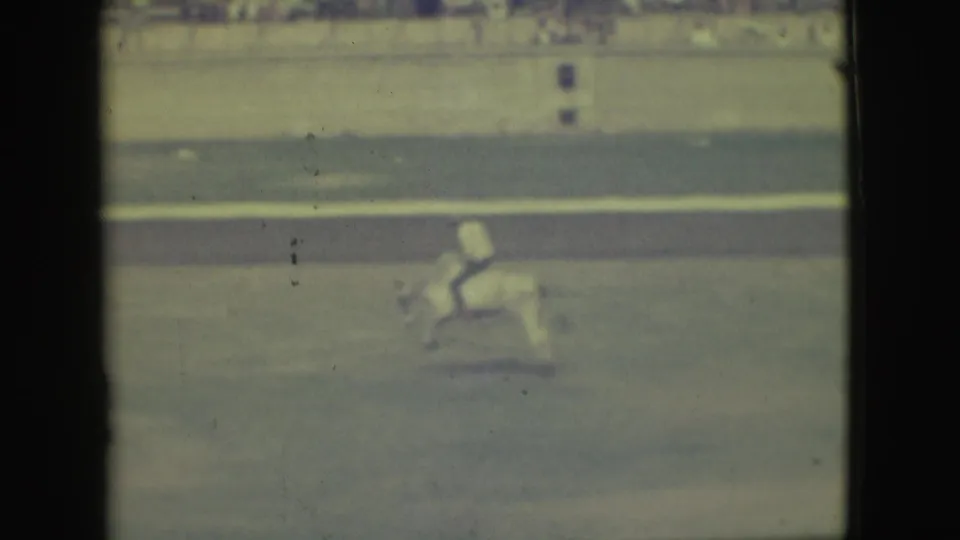 The rider continues across the Denver arena, seen through soft, faded 8mm color with spectators in the background.