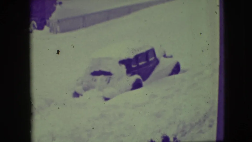 1945 Elmwood Park frame showing a dark car nearly buried in snow, with only the upper body and windows clearly visible.
