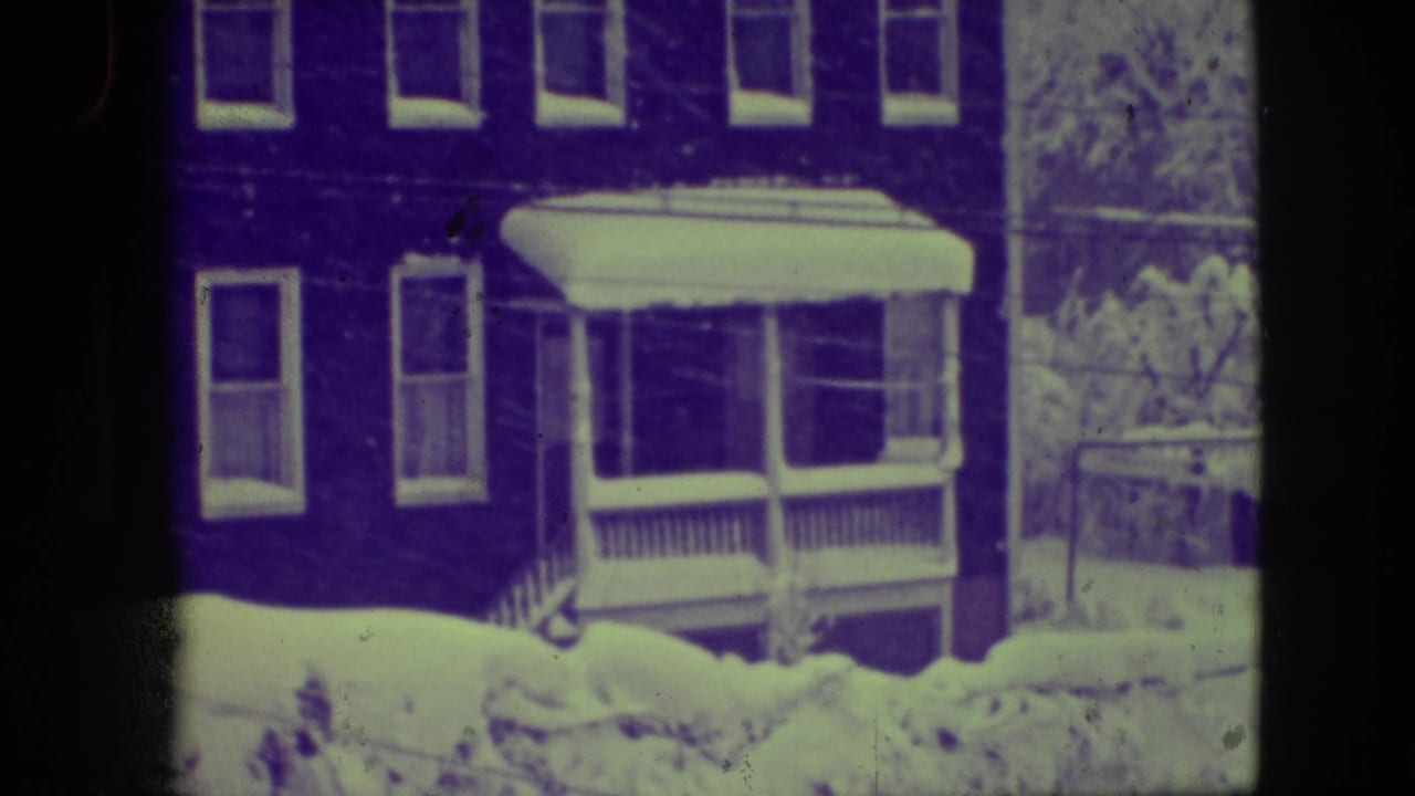 Snow-covered brick house with a covered porch and bare trees nearby.
