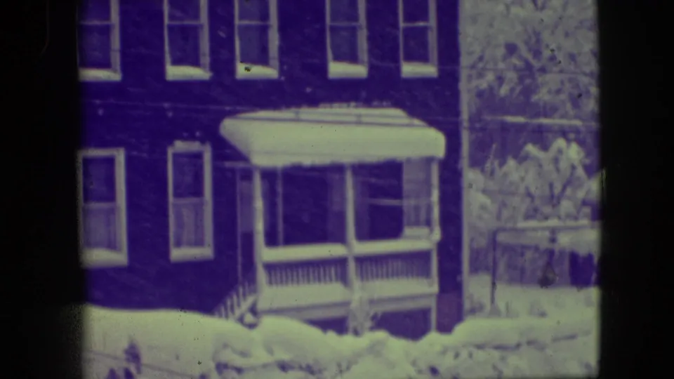 Elmwood Park winter frame from 1945 showing the same brick house and porch under snow with aged purple-green film coloration.