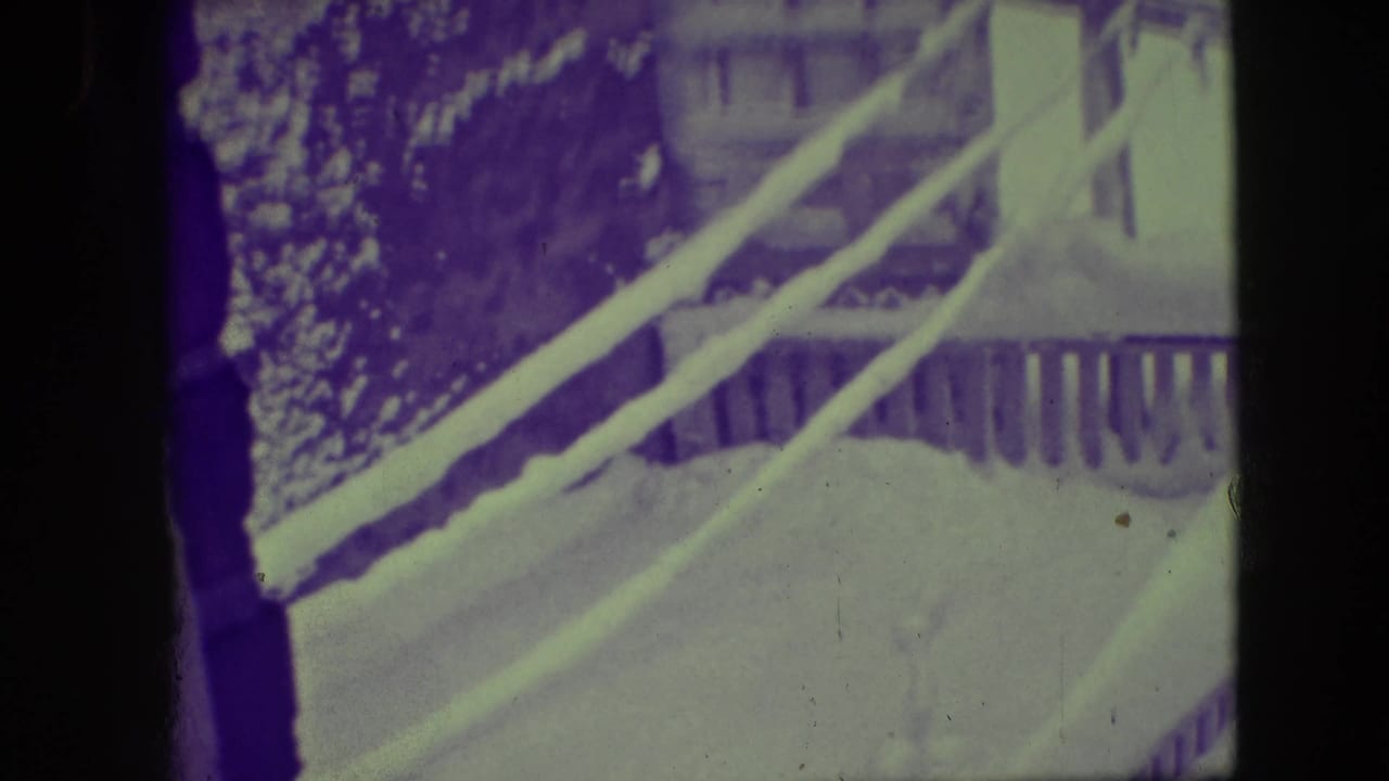 1945 Elmwood Park home-movie frame looking through a window at heavy snow, a railing, and residential exterior forms.