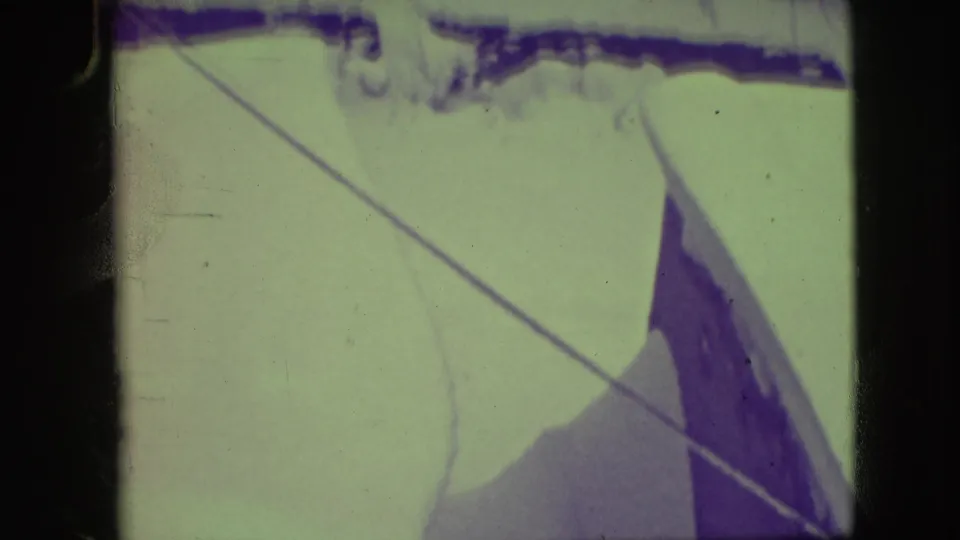1945 Elmwood Park home-movie frame with a diagonal rigging line crossing pale sail fabric under purple-green fading.