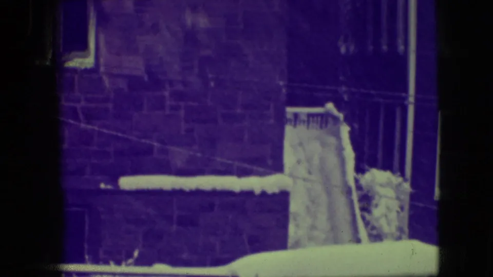 1945 Elmwood Park home-movie frame showing snow piled on a residential roof edge beside brick walls and windows, with aged 8mm color shift.