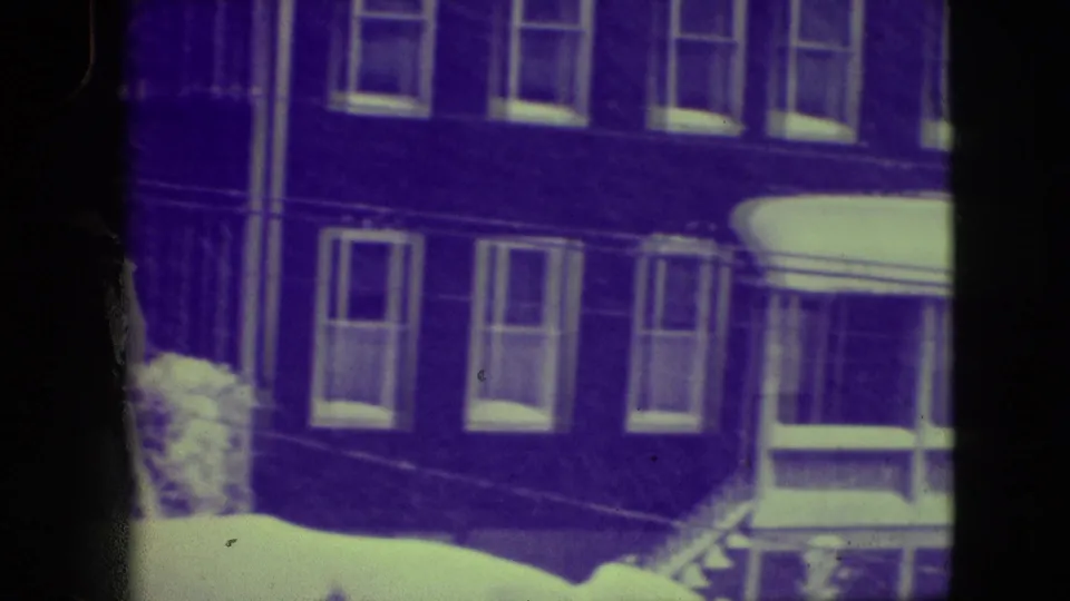 A snowy Elmwood Park residential exterior appears through aged 8mm film, with brick walls, upper windows, and a porch or enclosed entry at right.