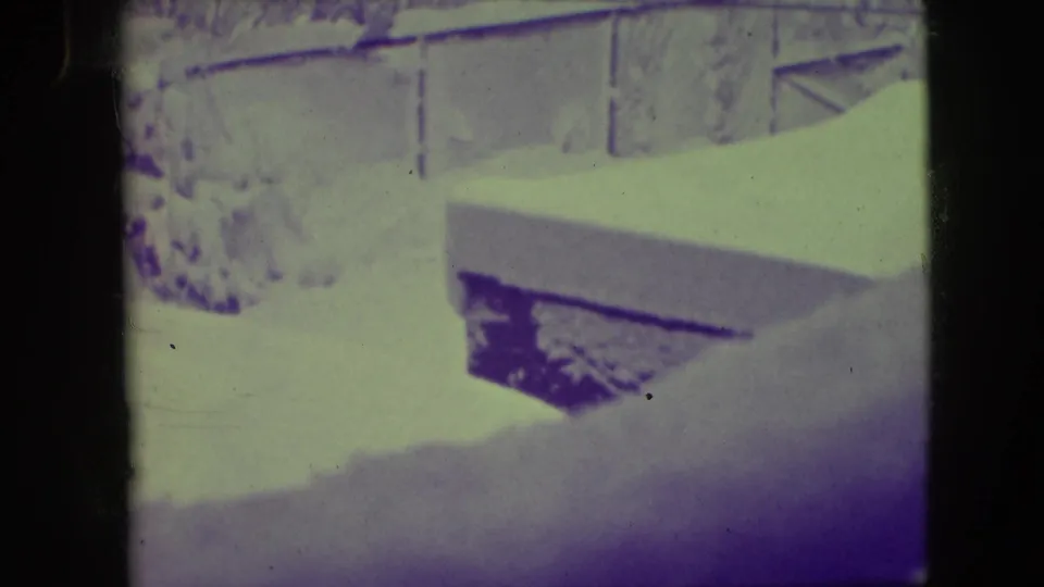 A 1945 Elmwood Park winter frame shows heavy snow on a roof or ledge, with brick residential surfaces and window details behind it.