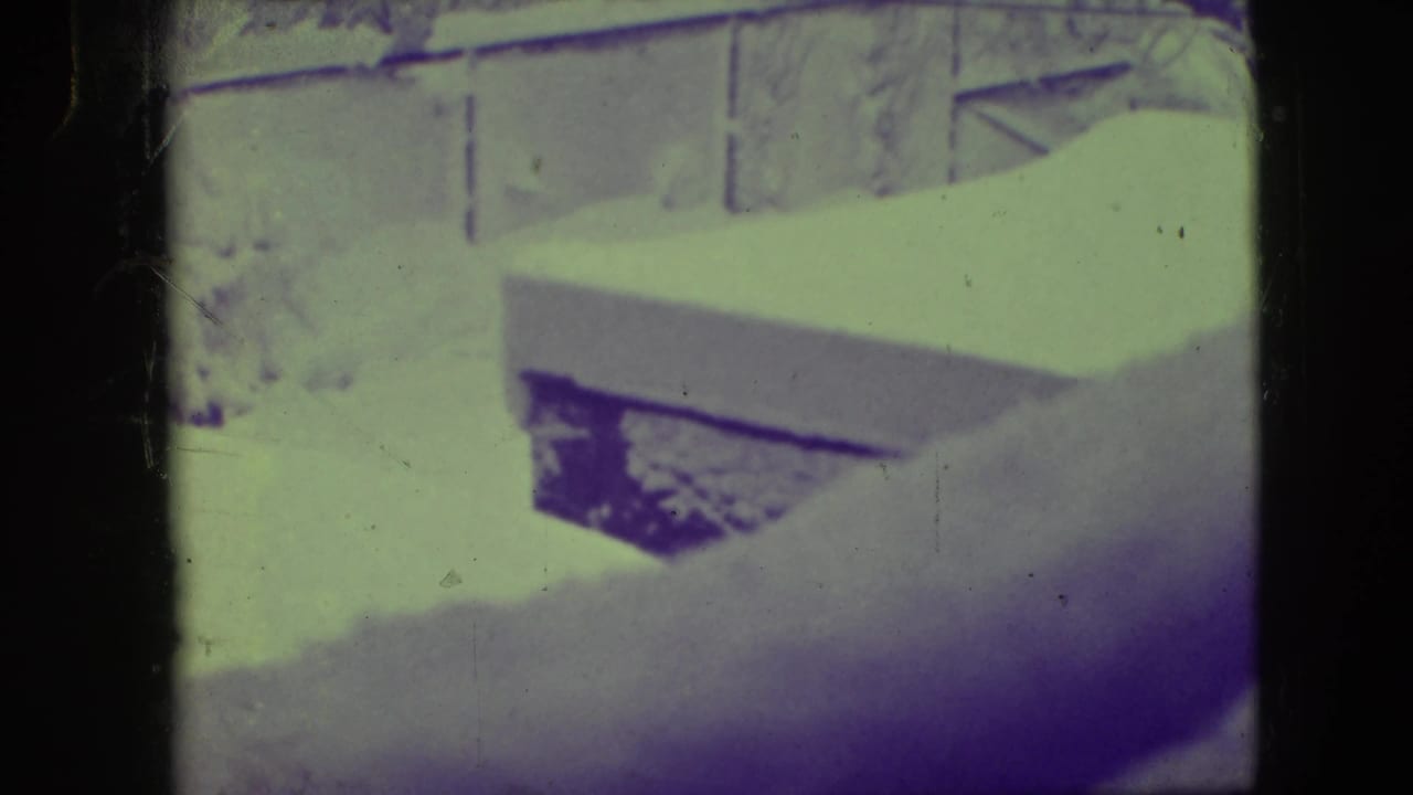 Snowy outdoor view with a wooden structure and dark film edges.