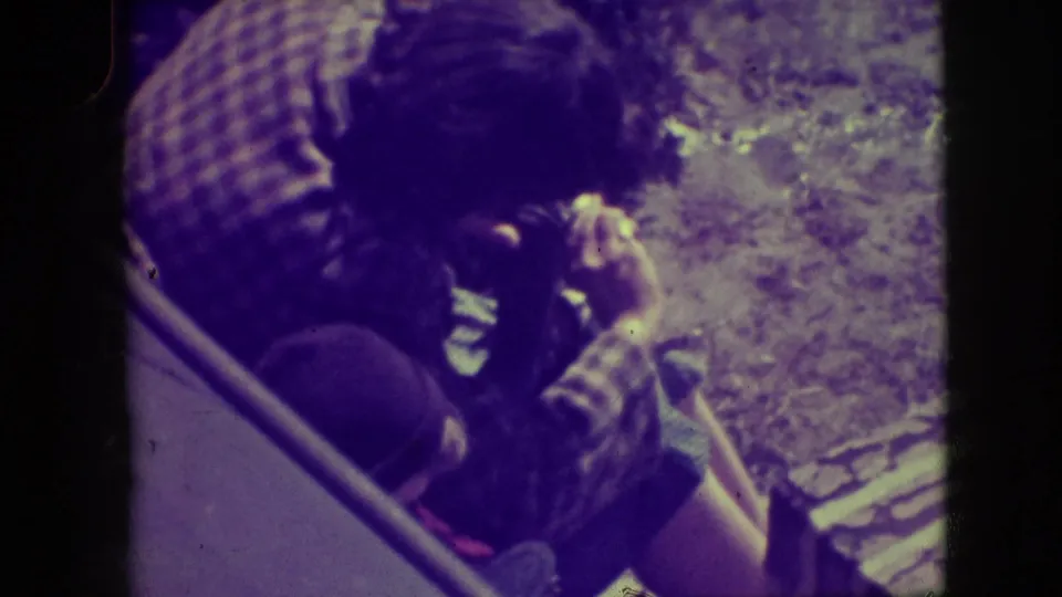 The man continues adjusting the camera as the 8mm frame shows winter ground and strong purple-green aging.
