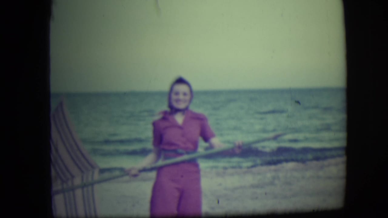 In Long Beach, New York, a woman in a pink outfit stands near the shore holding a long pole, with ocean waves behind her.