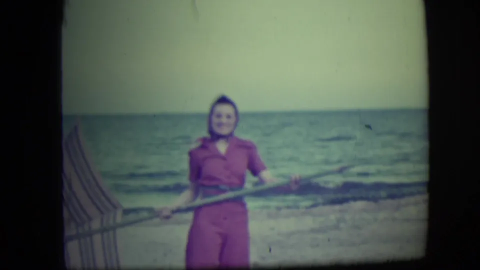In Long Beach, New York, a woman in a pink outfit stands near the shore holding a long pole, with ocean waves behind her.