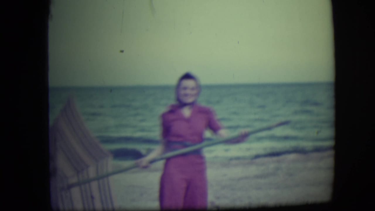 Woman on the beach smiling while holding a pole near the waterline.