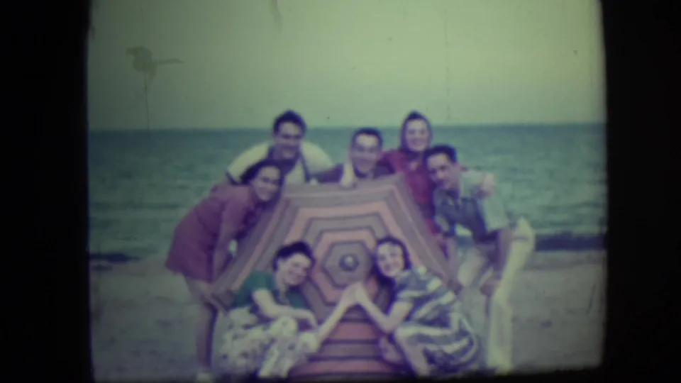 Seven adults gather around a patterned beach canopy on Long Beach, New York, posing together with the shoreline behind them.