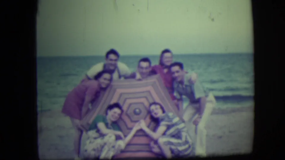 The Long Beach group continues posing around the patterned canopy, with several adults leaning toward the camera near the water.