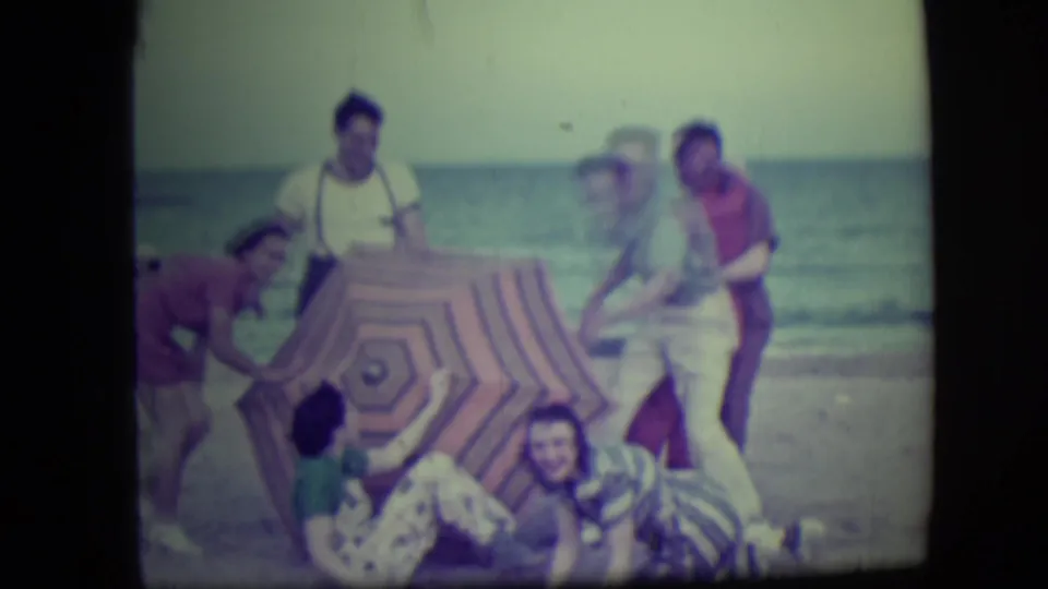 The Long Beach group starts to break from the pose, with several people leaning or falling beside the striped umbrella.