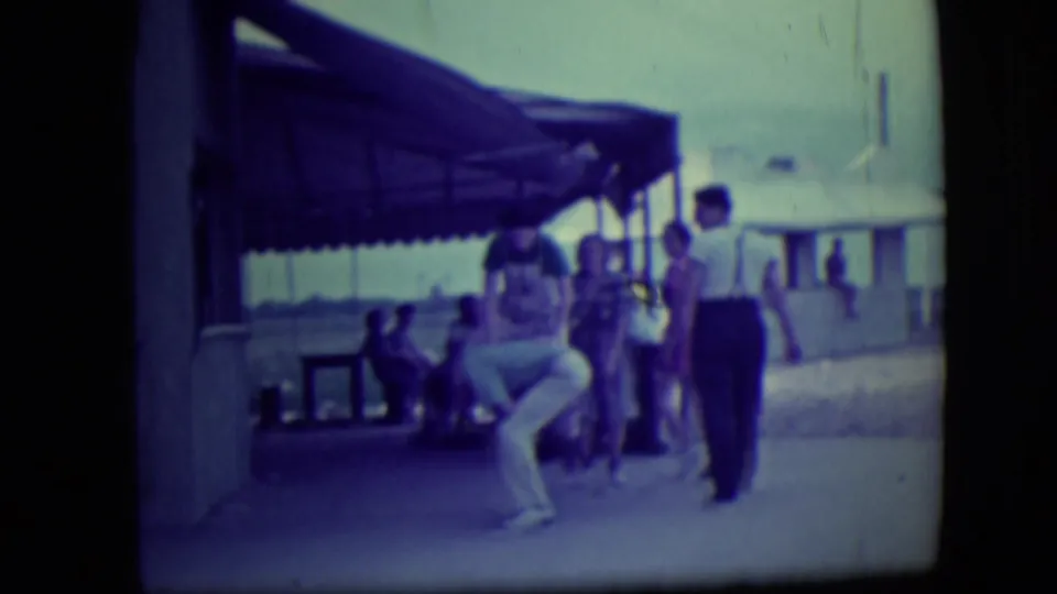 At a Long Beach shelter or boardwalk area, beachgoers stand and sit while one person moves near the camera.