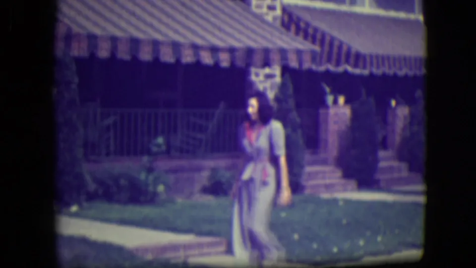 Woman walks across a River Forest front yard, with a brick house and striped awning visible behind her.