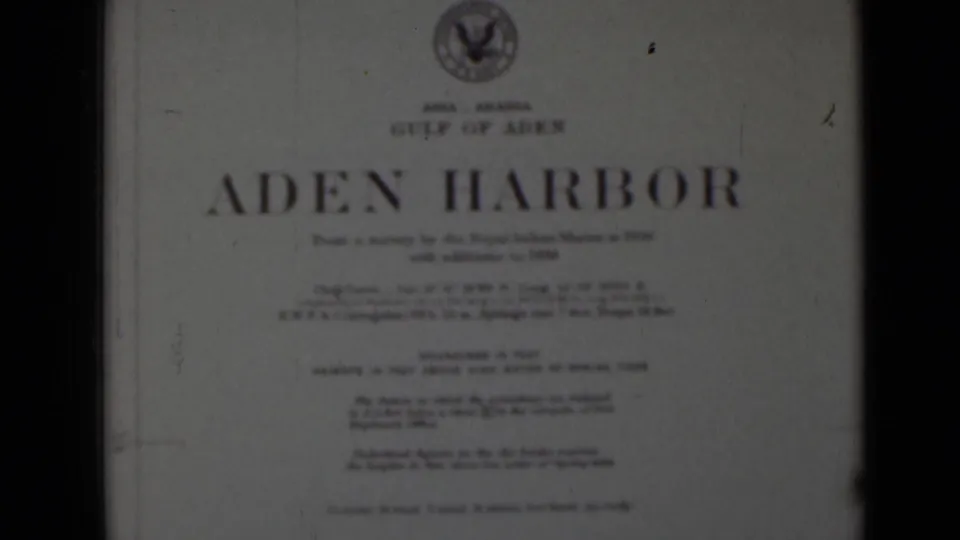 White Aden Harbor title card with large blue lettering, small survey text, top emblem, and visible 8mm frame edges.
