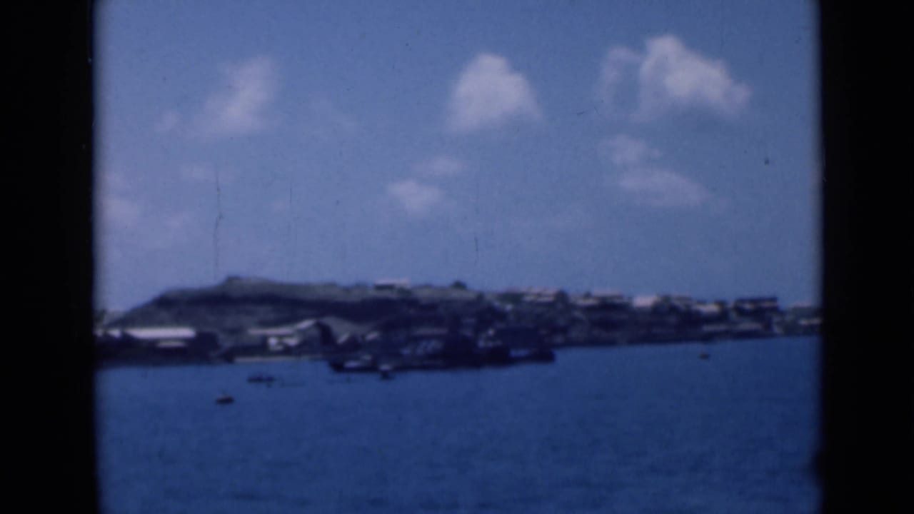 Soft 8mm view of a coastal settlement identified in metadata as Aden, Yemen, seen across calm blue harbor water in 1946.