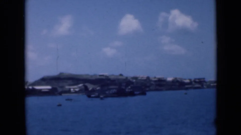 Soft 8mm view of a coastal settlement identified in metadata as Aden, Yemen, seen across calm blue harbor water in 1946.