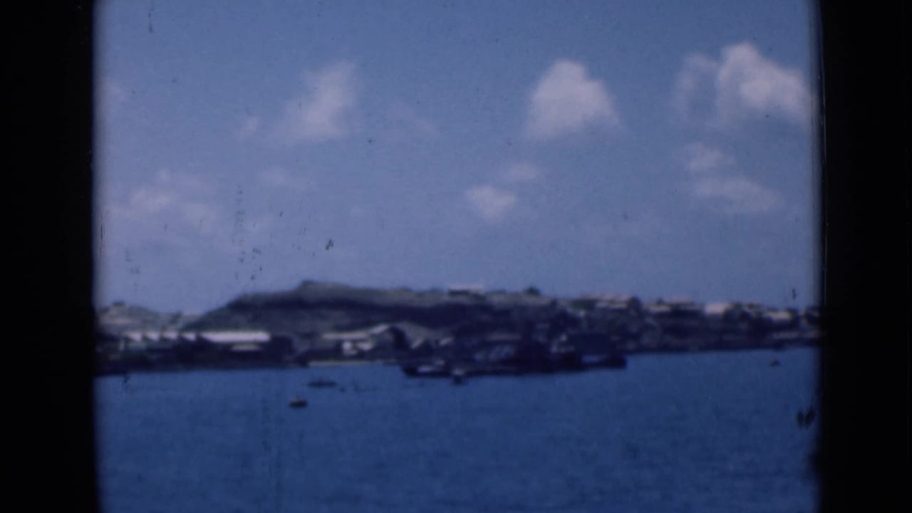 Harbor water with a distant built shoreline and clouds framed by dark film edges.
