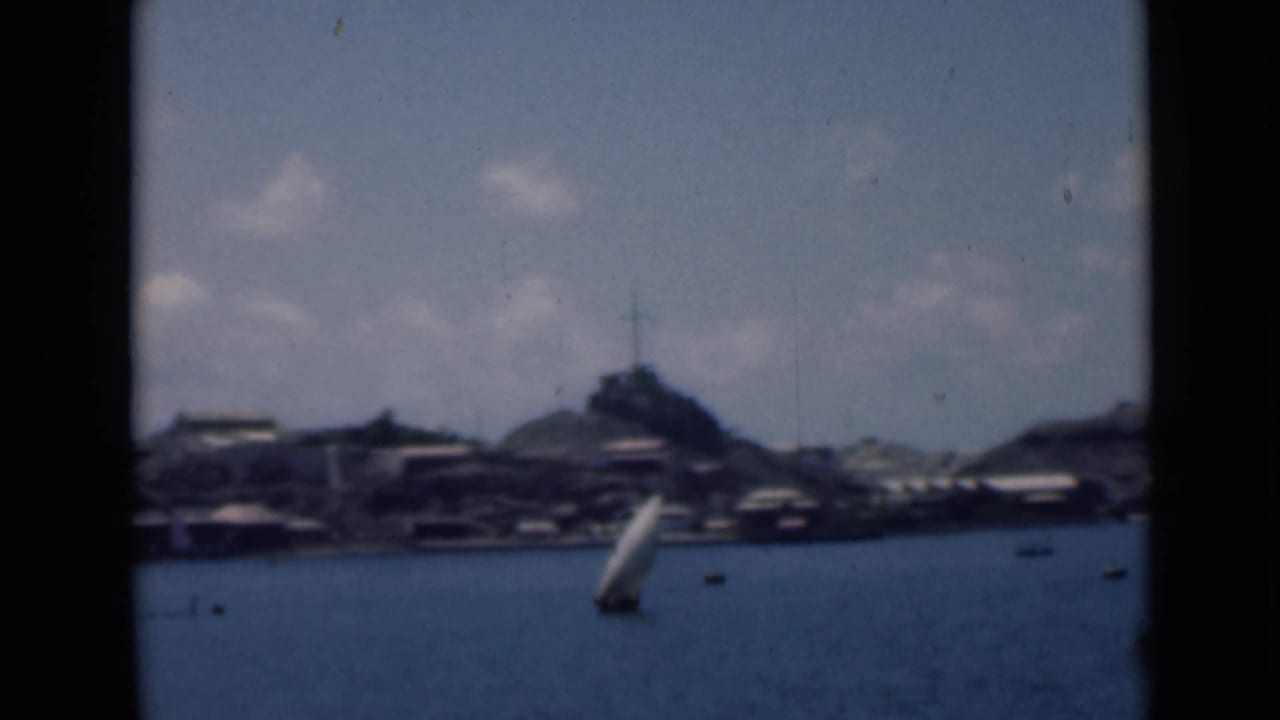 Distant bay shoreline with a small white sailboat and low buildings under scattered clouds.