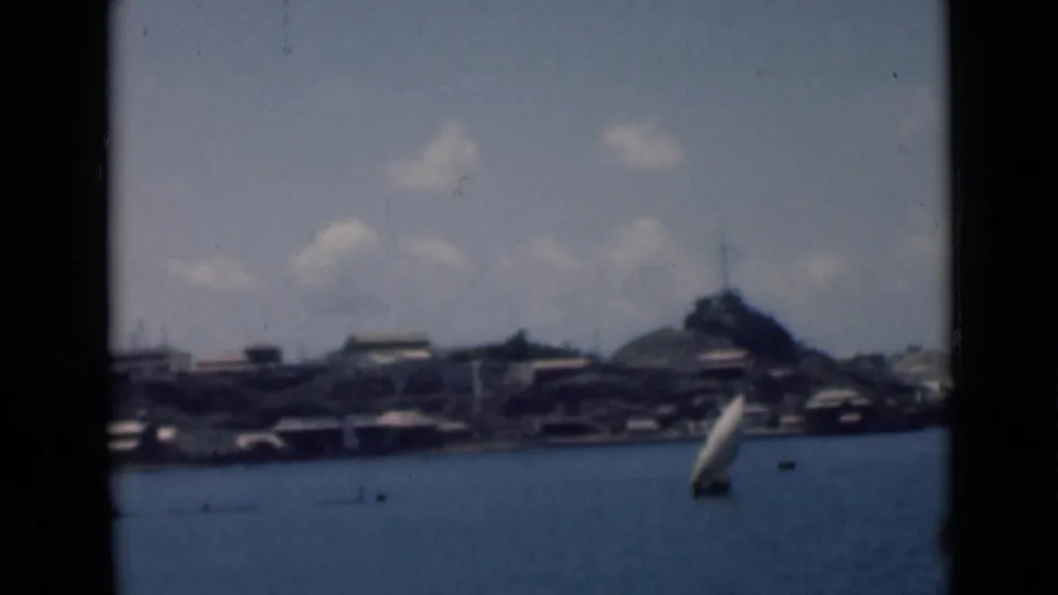 Soft 8mm frame of a coastal bay identified in metadata as Aden, Yemen, with a sailboat and distant waterfront buildings.