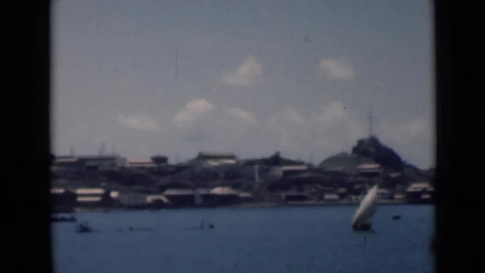 End frame from 1946 8mm bay footage, showing a small sailboat, distant shoreline buildings, and a hill under a partly cloudy sky.