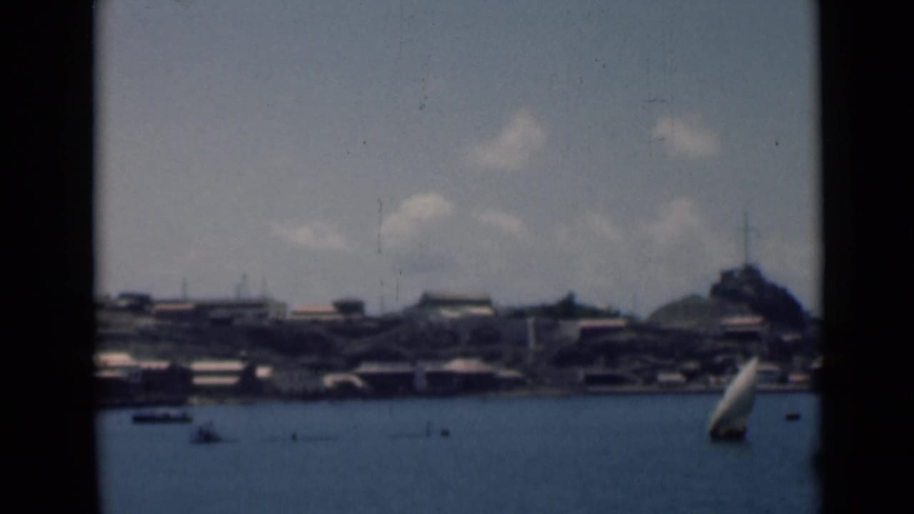 Harbor water with small boats below a distant hillside settlement and mountains.
