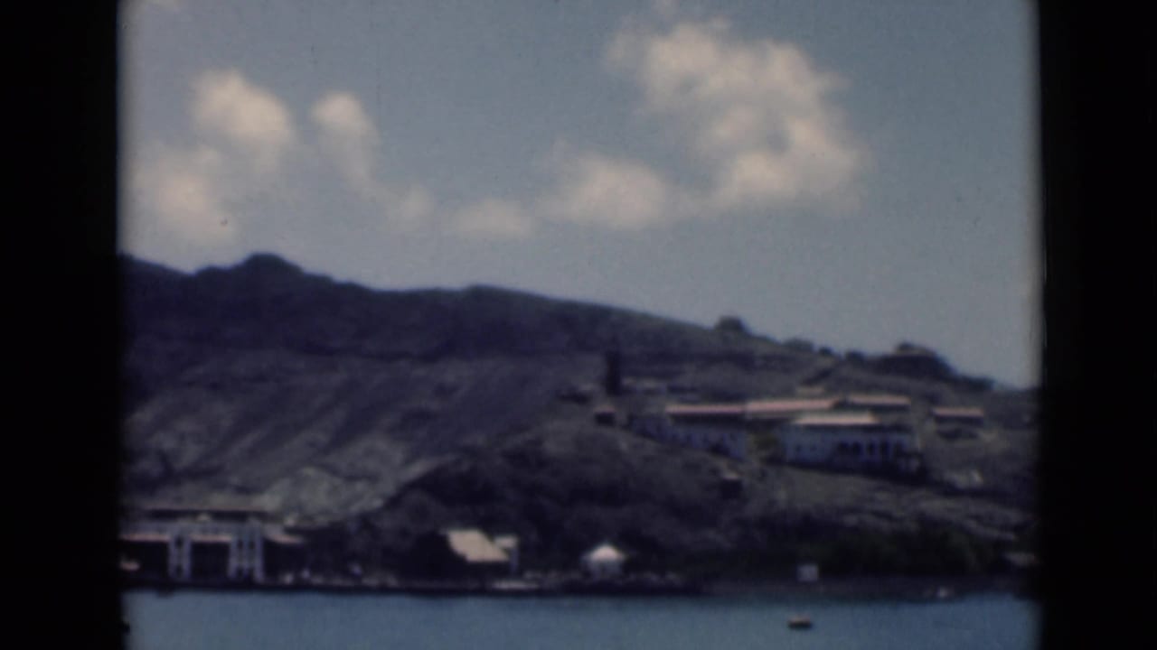 Rocky mountain slope and waterfront buildings seen across calm harbor water.