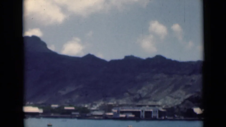 Soft 8mm view of a coastal settlement below a mountain ridge, with water in the foreground and no visible people.
