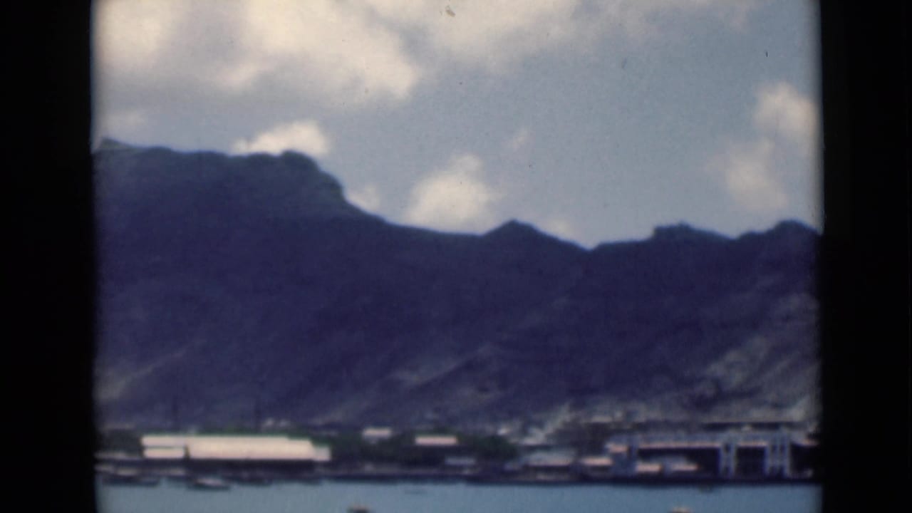 1946 8mm frame identified in metadata as Aden, Yemen, showing dark mountains above shoreline buildings and calm harbor water.