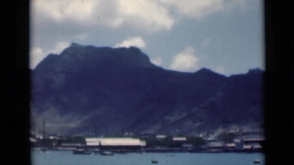 A soft 8mm view of a mountain-backed waterfront, with small boats and low buildings along the shore in footage labeled Aden, Yemen.
