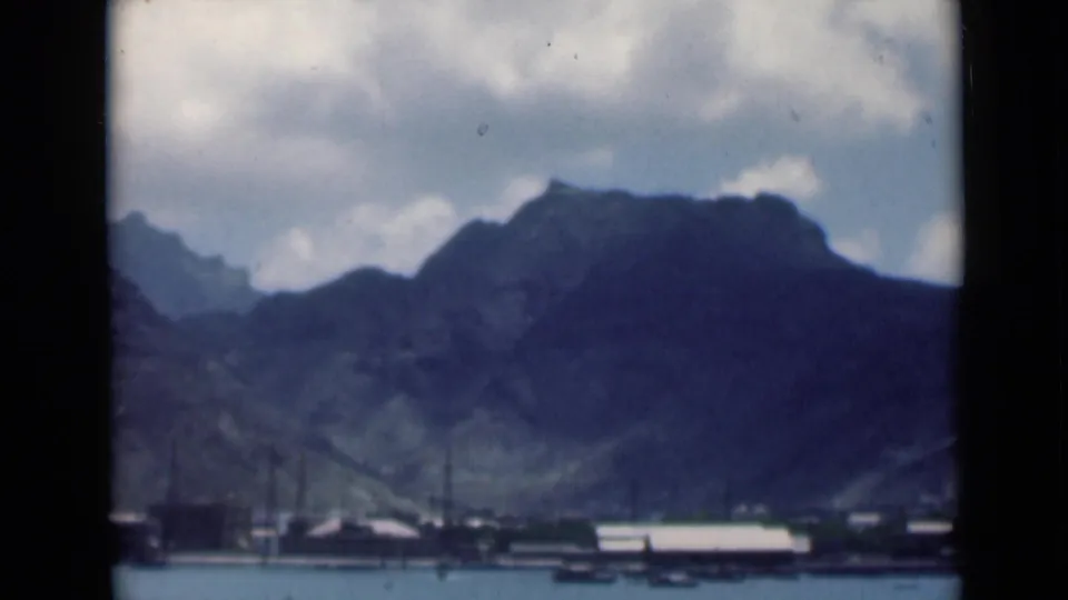 1946 8mm view of Aden, Yemen, showing a calm harbor, small boats, low shoreline structures, and rugged mountains beneath a cloudy sky.