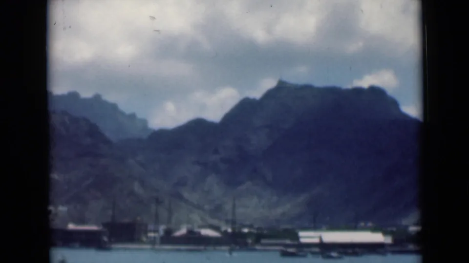 Aden harbor appears across the water, with small boats near the shoreline and dark mountain ridges filling the background.