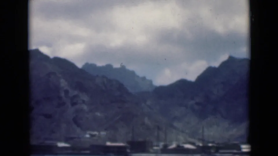 1940s 8mm view associated with Aden, Yemen, showing rugged mountains beyond a calm waterfront with tiny boats in the distance.