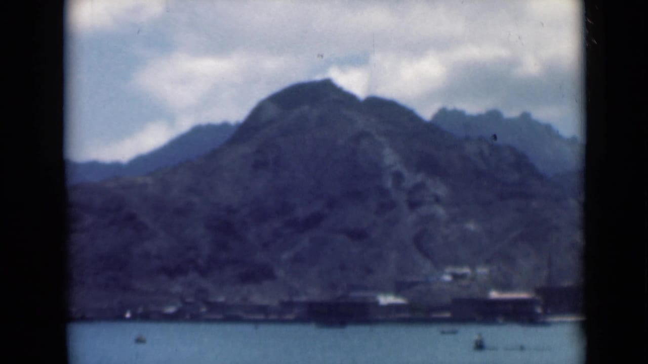 Mountain ridge and harbor water with small boats beneath a cloudy sky.