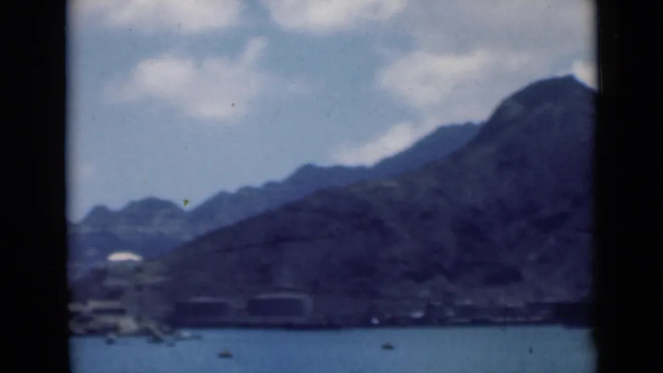 1946 8mm frame identified as Aden, Yemen in supplied metadata, showing blue water, boats, shoreline buildings, and rugged mountains.