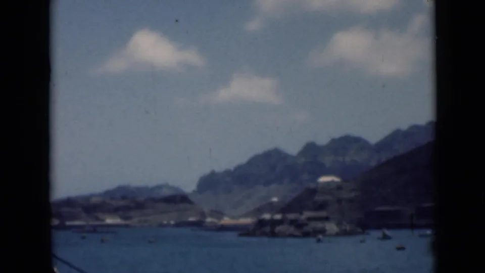 Vintage 8mm harbor view, likely from the supplied Aden context, with small vessels, waterfront structures, and mountainous coastline.