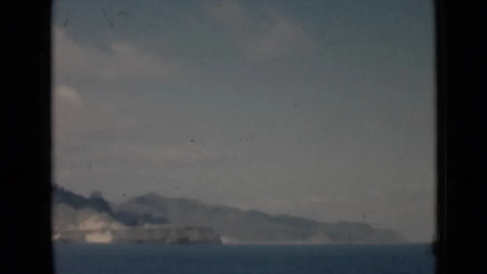 Soft 8mm coastal view with calm water, pale shoreline, distant hills, and hazy sky, consistent with the supplied Aden harbor context.