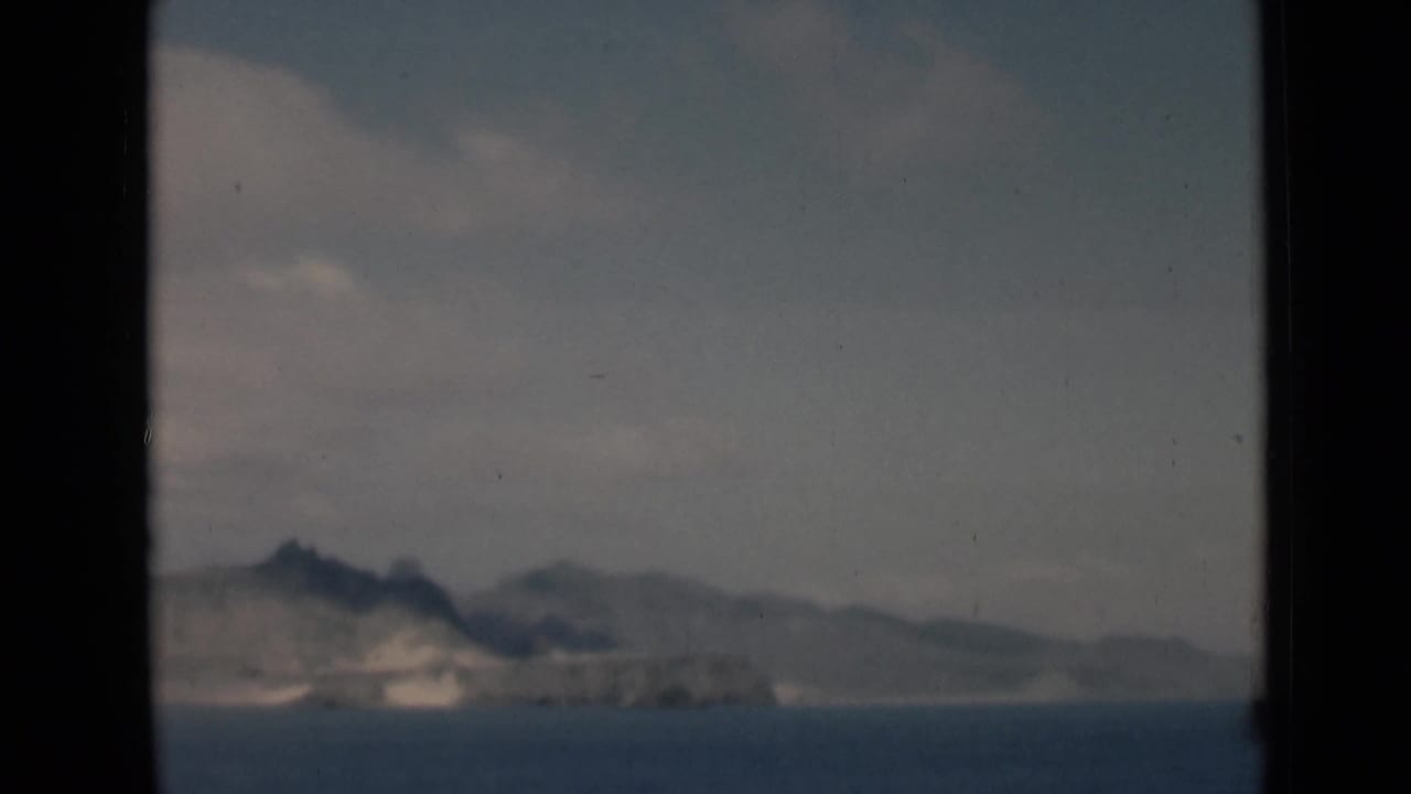 Rocky landform and low hills across blue water, seen through a dark film gate border.