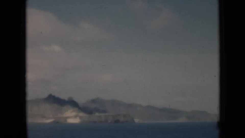 Distant coastal landform near Aden, Yemen, appears across blue water in a soft, grainy 8mm frame with muted clouds overhead.
