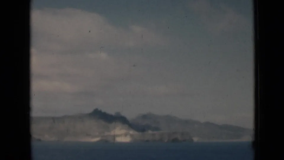 A distant rocky coastline near Aden, Yemen, sits beyond calm water in a grainy 1946 8mm home-movie frame with visible gate borders.