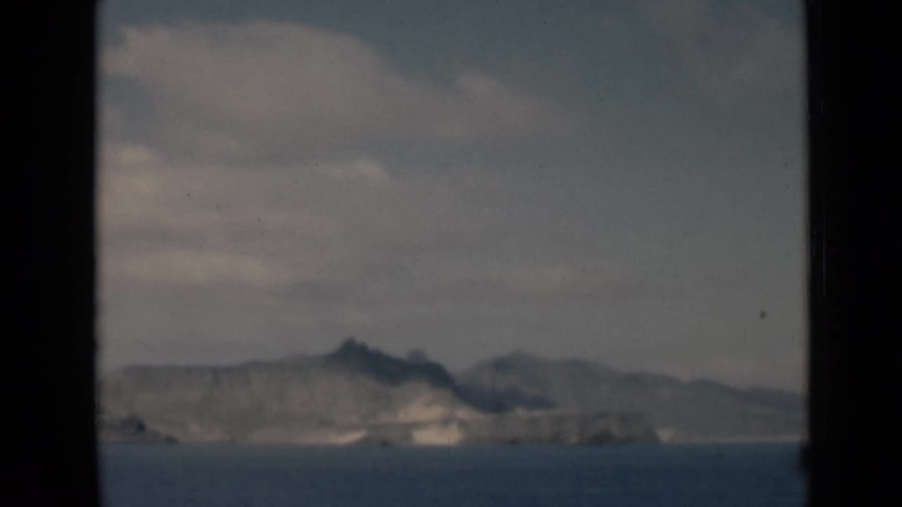 Distant rocky hills across calm water under a cloudy sky, framed by dark window edges.