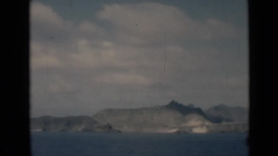 Mid-century 8mm landscape view of distant hills over calm water, bordered by dark edges and a cloudy sky.