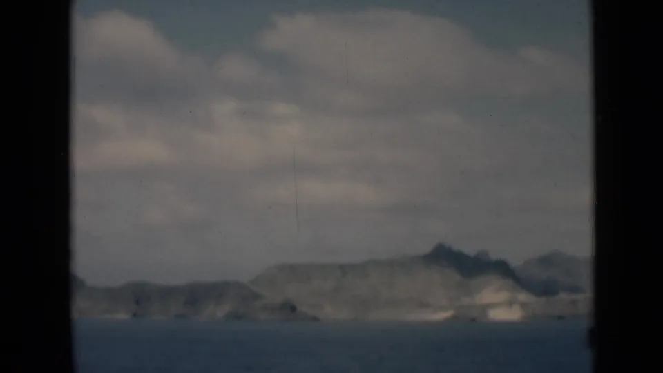 1946 8mm home-movie view of a distant Aden coastal cliffline across blue water, seen through dark frame borders.